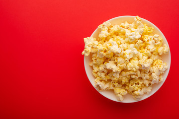 plate with popcorn on a red bright background. movie viewing concept, weekend getaway, with space