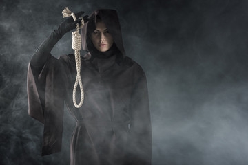 front view of woman in death costume holding hanging noose in smoke on black