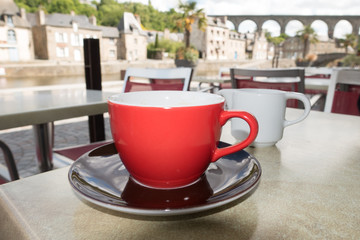 Close up of a red coffee cup and black saucer on a table top with bridge in background