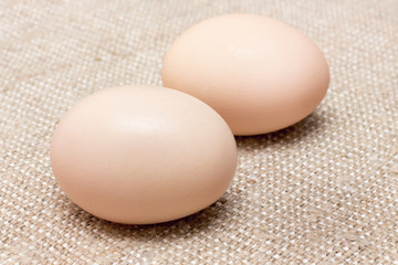 Two chicken eggs on a rough brown sack_