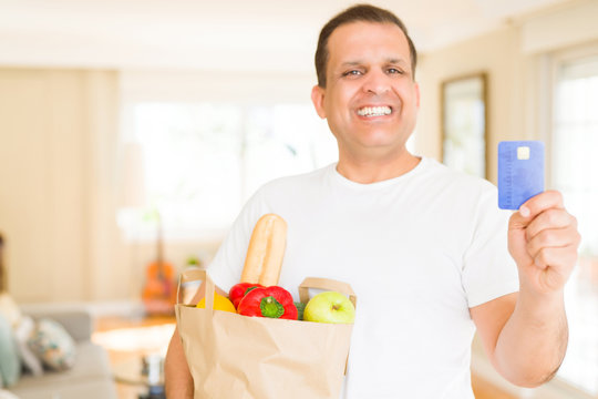 Middle age man holding groceries bag and showing credit card