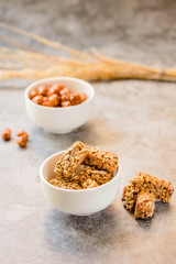 Gozinaki bars (Georgian Christmas confection) made of sunflower seeds and honey. Peanuts in sugar in white bowl and on gray background.Selective focusHealthy sweet dessert snack concept.