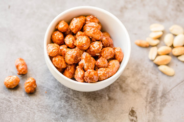 Peanuts in sugar in white bowl and on gray background. Sweet dessert snack concept