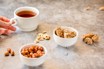 Gozinaki bars (Georgian Christmas confection) made of sunflower seeds and honey. Peanuts in sugar in white bowl and on gray background..The process of eating. In the hands of a young woman.