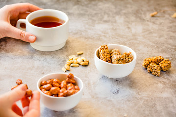 Gozinaki bars (Georgian Christmas confection) made of sunflower seeds and honey. Peanuts in sugar in white bowl and on gray background..The process of eating. In the hands of a young woman.Close-up.