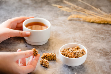 Gozinaki bars (Georgian Peanuts in sugar in white bowl and on gray background.The process of eating. In the hands of a young woman.Tea time concept