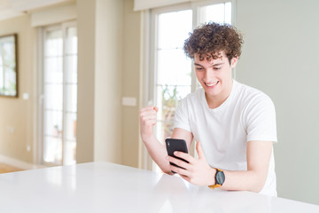 Young man using smartphone at home screaming proud and celebrating victory and success very excited, cheering emotion