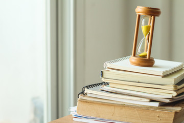 Yellow Sand running through the bulbs of an hourglass with stack book and document on office desk.Copy space. - Powered by Adobe