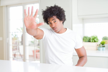 Young african american man wearing casual white t-shirt sitting at home doing stop sing with palm of the hand. Warning expression with negative and serious gesture on the face.