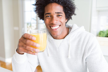 African American man holding and drinking glass of orange juice with a happy face standing and...