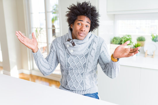 African American man wearing winter sweater clueless and confused expression with arms and hands raised. Doubt concept.