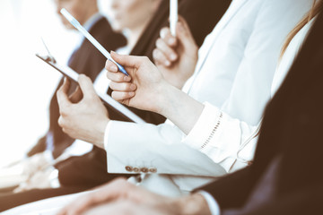 Business people working at meeting or conference, close-up of hands. Group of unknown businessmen and women in modern white office. Teamwork or coaching concept