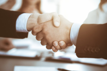 Business people shaking hands at meeting while theirs colleagues clapping and applauding. Group of unknown businessmen and women in modern white office. Success teamwork, partnership and handshake