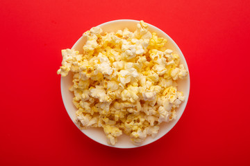plate with popcorn on a red bright background. movie viewing concept, weekend getaway, with space
