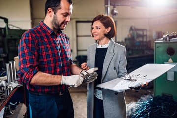 Machinist standing with female engineer and measuring cogwheel diameter