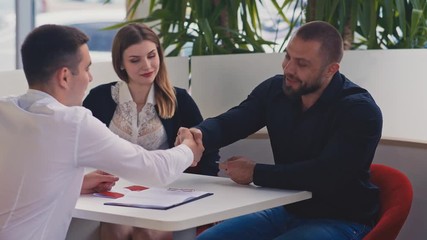Beautiful couple in car dealership. Young salesman giving keys of car to buyer. Men shaking hands in car dealership