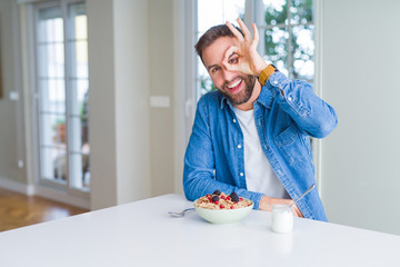 Handsome man eating cereals for breakfast at home doing ok gesture with hand smiling, eye looking through fingers with happy face.