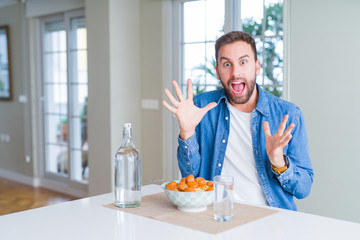 Handsome man eating pasta with meatballs and tomato sauce at home celebrating crazy and amazed for success with arms raised and open eyes screaming excited. Winner concept