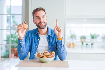 Handsome man eating chocolate chips muffin surprised with an idea or question pointing finger with happy face, number one