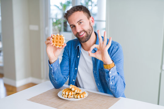 Handsome man eating sweet Belgian pancakes doing ok sign with fingers, excellent symbol
