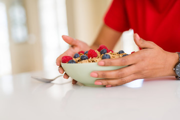 Close up of young woman eating healthy cereals and berries for breakfast