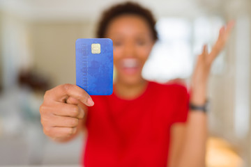 Young african american woman holding credit card very happy and excited, winner expression celebrating victory screaming with big smile and raised hands