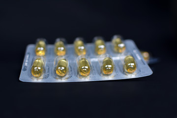 Blister pack with yellow pills fille with liquid medicine on black studio background