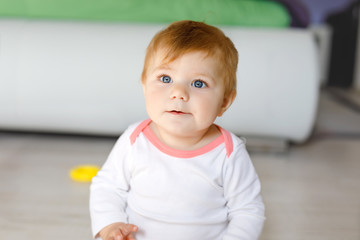 Fototapeta premium Adorable baby girl playing with educational toys in nursery. Happy healthy child having fun with colorful different toys at home. Kid trying to build plastic pyramid and using blocks with letters