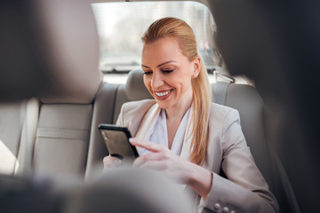 Positive female executive using phone on the back seat of the car.