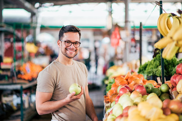 Portrait of a smiling millennial man buying fruit on market.