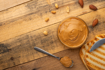 bowls of peanut butter and peanuts on a dark wooden background from top view, rich breakfast