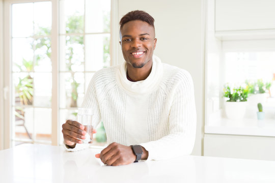 African american man driking a fresh glass of water with a happy face standing and smiling with a confident smile showing teeth