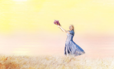 A girl whirling with a bouquet of wild flowers in her hands among the grass on a cliff by the sea. The atmosphere of happiness and carelessness.
