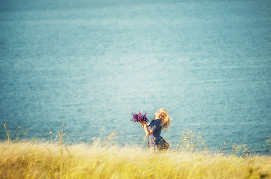 A girl whirling with a bouquet of wild flowers in her hands among the grass on a cliff by the sea. The atmosphere of happiness and carelessness.