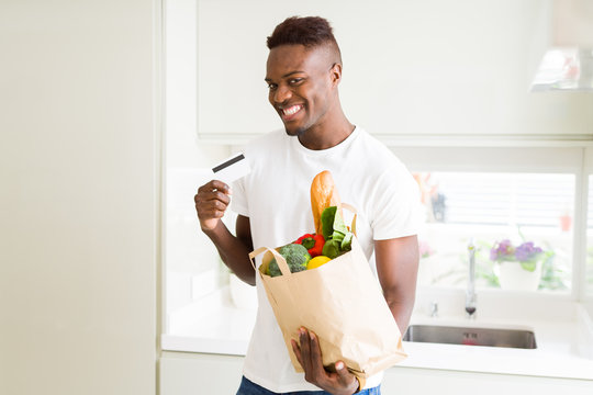 African american man holding paper bag full of groceries and holding credit card as payment