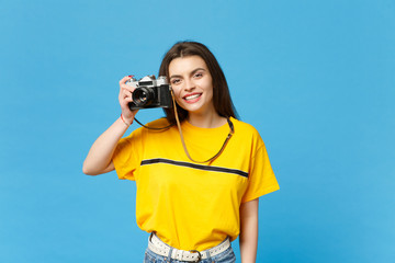 Portrait of smiling young woman in vivid casual clothes take pictures on retro vintage photo camera isolated on bright blue wall background in studio. People lifestyle concept. Mock up copy space.