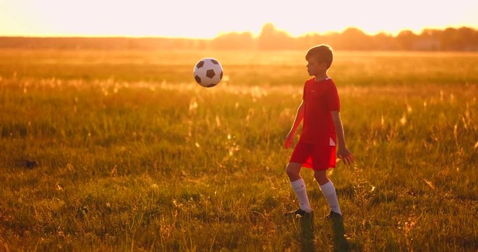 Boy football player at sunset juggling the ball in the field