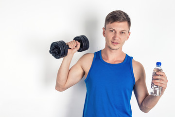 Handsome young man in blue shirt holding a dumbbell and a water bottle. White background