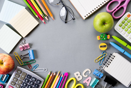 Education or back to school Concept. Top view of Colorful school supplies with books, color pencils, calculator, pen cutter clips and green apple on gray background. Flat lay.