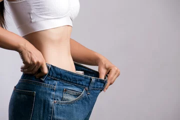 Poster Young slim woman in oversized blue jeans. Fit woman wearing too large pants. Healthcare and woman diet lifestyle concept to reduce belly and shape up healthy stomach muscle. © Siam