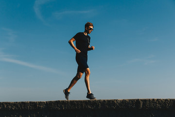 Fototapeta premium Young running man on sky background at sunrise