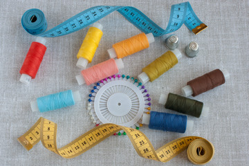Fototapeta na wymiar sewing tools: colored threads for sewing, centimeter ribbons, thimbles and colored pins on a light gray background close-up, copy space