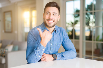 Young handsome man at home pointing and showing with thumb up to the side with happy face smiling