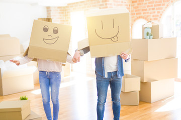 Fototapeta na wymiar Couple having fun at new apartment wearing boxes with funny faces over head