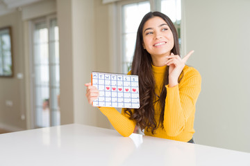 Young woman holding menstruation calendar very happy pointing with hand and finger to the side