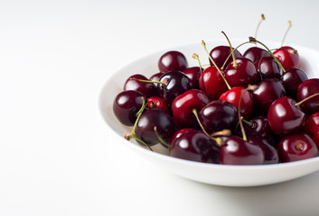 Cherry in white dish. A bunch of juicy ripe sweet cherries in a white plate on a white background. Fresh red berries contrast with the white table.