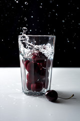 Cherry in the water. Glass filled with water and cherries. Red berry dropped into the water. Splashes and drops on a black background. Glass of water with cherry