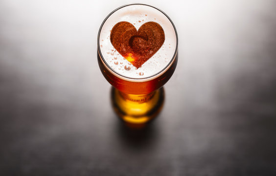 Loving beer concept. Heart symbol on beer glass foam on black table, view from above