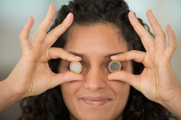 headshot of woman holding coins over her eyes