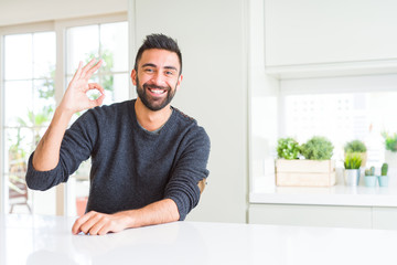 Handsome hispanic man wearing casual sweater at home smiling positive doing ok sign with hand and fingers. Successful expression.